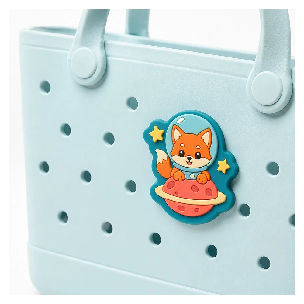 Close-up of a die-cut soft PVC astronaut fox bag charm on a blue tote