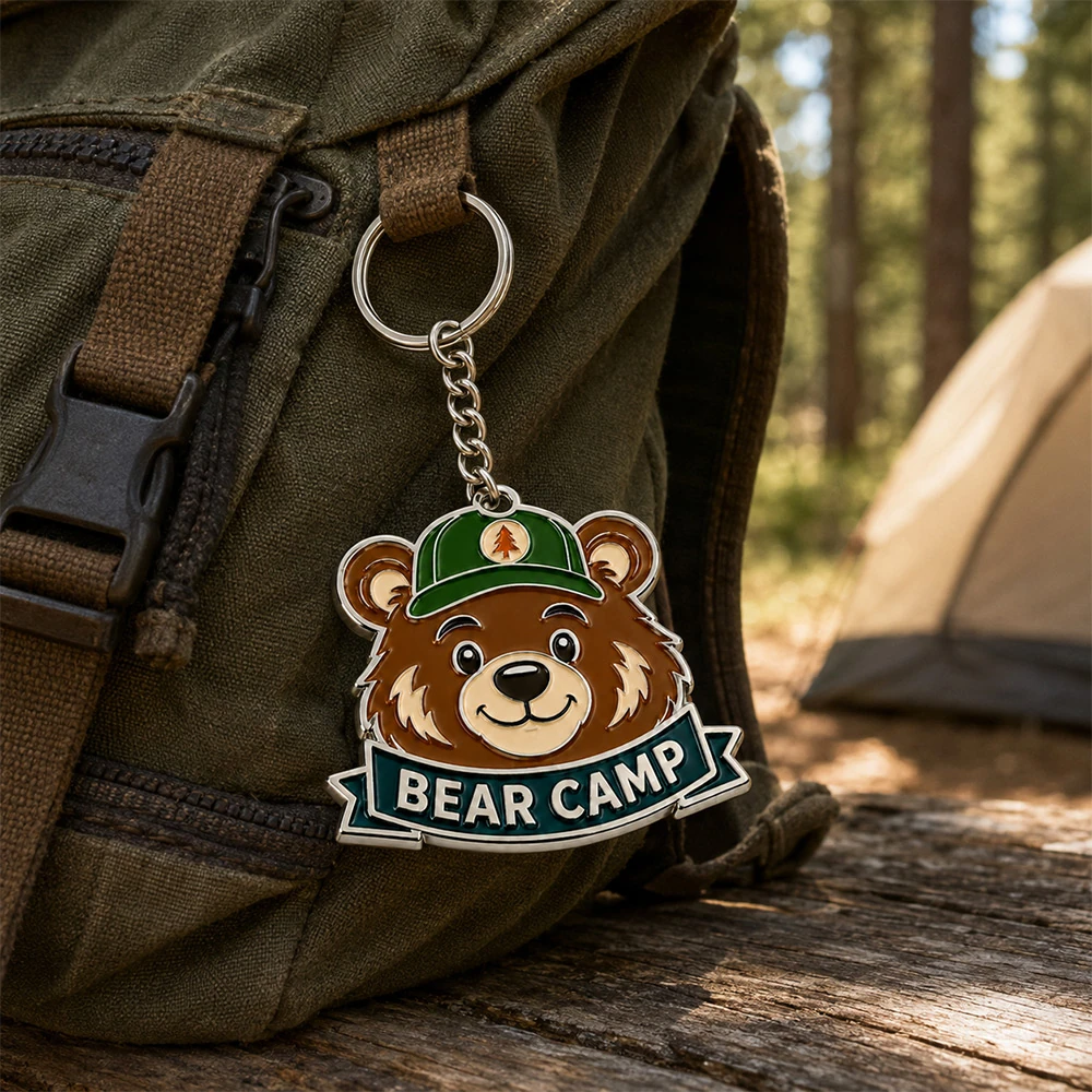 Bear camp soft enamel keychain clipped to a canvas backpack at a campsite